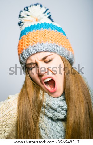 Happy beautiful girl yawns funny, knit cap, winter concept, photo studio, portrait of a woman isolated on gray background