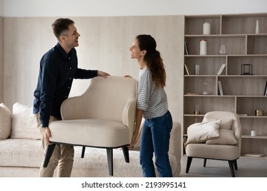 Happy beautiful hispanic young family couple homeowners holding armchair, enjoying renovating living room rearranging furniture together. Smiling spouses relocating on moving day into own dwelling.