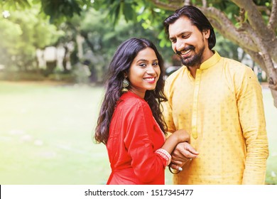 Happy beautiful indian couple wearing traditional clothes holding hands in the park