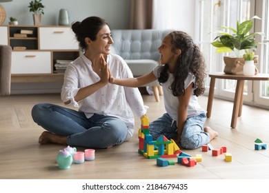 Happy beautiful Indian mom and pretty little daughter girl clapping hands, giving high five over wooden construction blocks, toy tower, castle on heating floor, celebrating model completing - Powered by Shutterstock