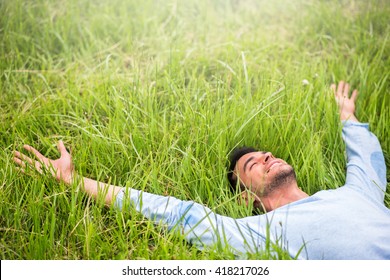 Happy beautiful man lying on the green grass with arms outstretched