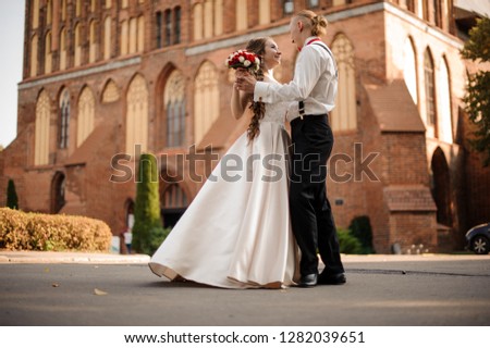 Happy and beautiful married couple dancing in the background of vintage red brick building on sunny day