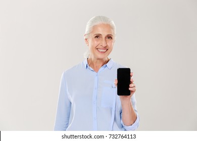 Happy Beautiful Mature Woman In Blue Shirt Showing Smartphone With Blank Black Screen Isolated