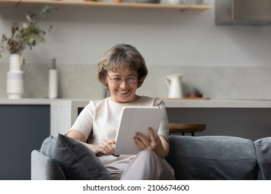 Happy beautiful middle aged old woman in eyewear using digital computer tablet apps, laughing watching funny photo video content in social networks, communicating online or shopping in internet store.