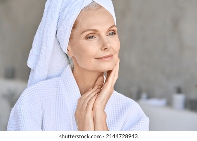 Happy beautiful middle aged woman wearing bathrobe and white towel with perfect complexion touching face looking away in bathroom. Advertising of skin care spa wellness concept. Closeup portrait. - Powered by Shutterstock