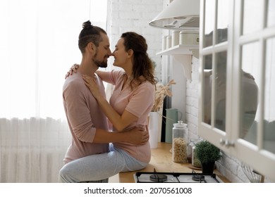 Happy beautiful millennial married family couple cuddling, touching noses showing sincere loving tender feelings at home, spending romantic affectionate dating time together in modern kitchen.