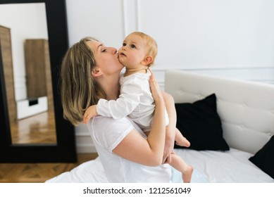 Happy Beautiful Mommy Holding The Baby And Kissing The Baby On The Cheek. 