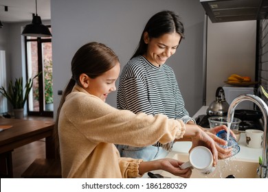 Happy beautiful mother and daughter smiling and washing dishes in cozy kitchen - Powered by Shutterstock