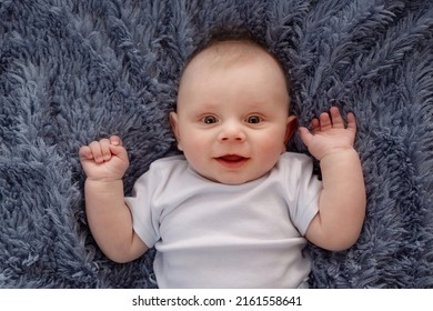 Happy Beautiful Newborn Baby Boy Lying On His Back On A Blue Background. Portrait Beautiful Newborn Looks Into The Frame