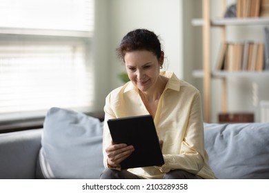 Happy beautiful old mature retired woman using digital touchpad gadget, communicating in social network, shopping online, web surfing information or playing games, sitting on comfortable sofa. - Shutterstock ID 2103289358