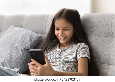 Happy beautiful pre teen girl kid browsing social media on smartphone, chatting online, playing virtual game on Internet, resting on sofa, enjoying leisure, online communication - Powered by Shutterstock