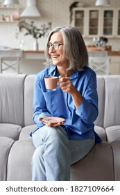 Happy Beautiful Relaxed Mature Older Adult Grey-haired Woman Drinking Coffee Relaxing On Sofa At Home. Smiling Stylish Middle Aged 60s Lady Enjoying Resting Sitting On Couch In Living Room, Vertical.