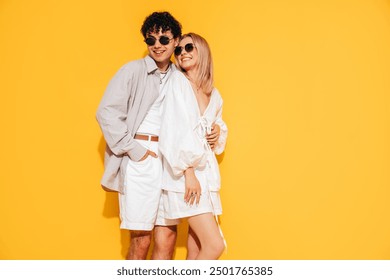 Happy beautiful romantic teenage couple. Smiling handsome caucasian man and young woman in summer clothes posing in studio, hugging sharing emotions, cheerful and happy. Isolated on yellow, sunglasses - Powered by Shutterstock