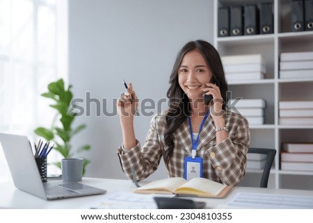 Happy beautiful smiling Asian businesswoman talking on mobile phone while working in office.