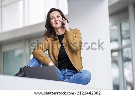 happy beautiful student woman working remotely infront of a notebook in casual jeans outfit in a modern university lobby on a white background
