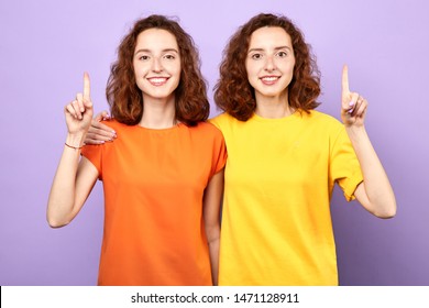 Happy beautiful twins girls point up isolated on blue background, two sisters showing something above their heads , advertisement, place for text, body language