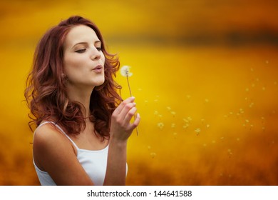 Happy Beautiful Woman Blowing Dandelion In The Field