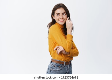 Happy Beautiful Woman In Casual Clothes, Looking At Empty Space At Left Side, Smiling And Touching Clean Soft Face, Standing Against White Background.