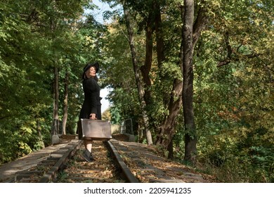 Happy Beautiful Woman With Closed Eyes In Black Hat, Classic Jacket And On Old Suitcase In Hand. Autumn Forest. Back View.