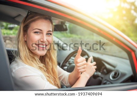 Happy beautiful woman is driving a red car.