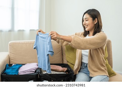Happy Beautiful woman to folding her clothes pack suitcase for travel in holiday. Young female folding clothes while packing luggage at home. - Shutterstock ID 2310743981