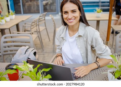 Happy beautiful woman with laptop near hi-tech business building. She drinks coffee in to go cup and enjoy summer warmth. Space for text