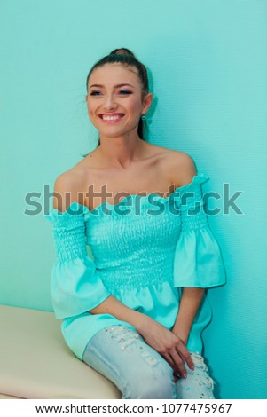 Happy beautiful woman with make up sitting near bright blue wall