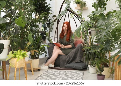 Happy Beautiful Woman Reading Book In Egg Chair At Home