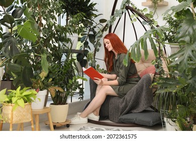 Happy Beautiful Woman Reading Book In Egg Chair At Home