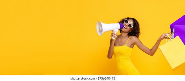 Happy beautiful woman with shopping bags and megaphone on isolated colorful yellow banner background for sale and discount concepts
