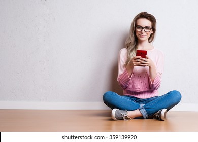 Happy beautiful woman sitting on the floor and using smartphone - Shutterstock ID 359139920