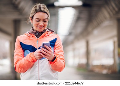 Happy Beautiful Woman In Sportswear Using Smartphone During Training Outside In The Winter. Healthy Lifestyle, Winter Fitness, Cold Weather.