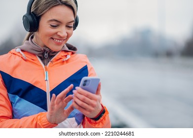 Happy Beautiful Woman In Sportswear Using Smartphone During Training On The Bridge At Winter. Healthy Lifestyle, Winter Fitness, Cold Weather.