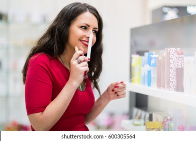 Happy Beautiful Woman Testing Perfumes In Cosmetics Store