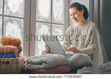 Happy beautiful woman watching videos or enjoying entertainment content on a laptop sitting near windows in the house in the winter. 