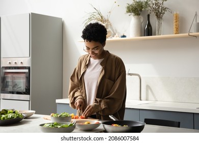 Happy Beautiful Young 30s African American Woman In Eyeglasses Chopping Fresh Vegetables For Salad On Countertop, Enjoying Cooking Vegan Food In Kitchen, Healthcare Hobby Activity, Dieting Concept.