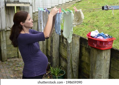 Happy Beautiful Young Adult Pregnant Housewife Woman (age 25-35) Doing Housework Pegging Out Washing To Dry On Clothes Line During Pregnancy. Real People . Copy Space