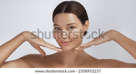 Happy beautiful young adult woman touching her perfect face with healthy shiny skin, hands on chin. Beauty photo of gorgeous girl after morning beauty cosmetic routine finishes daily makeup on pink