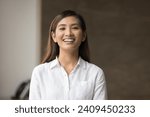 Happy beautiful young Asian manager woman in white formal shirt posing indoors, looking at camera, smiling, showing white perfect teeth. Successful female business leader head shot portrait