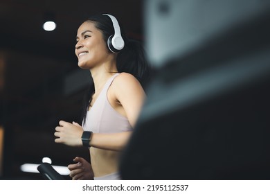 Happy beautiful young asian woman running on treadmill and listening to music via headphones during sports training in a gym. - Powered by Shutterstock