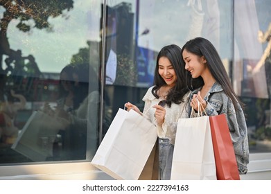 Happy and beautiful young Asian woman enjoy shopping with her friend, checking her purchases in a shopping bags, walking along the mall building. Urban and shopping lifestyle concept