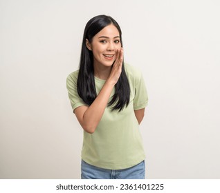 Happy beautiful young asian woman whispering some secret gossip. Excited pretty latin girl index finger on mouth standing pose on isolated white background.