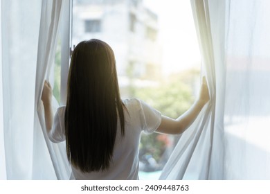 Happy Beautiful young Asian woman opening window curtain in the morning. Portrait of Pretty Asian young woman looking the sun rise outside through the window peacefully, Asian girl portrait close up. - Powered by Shutterstock