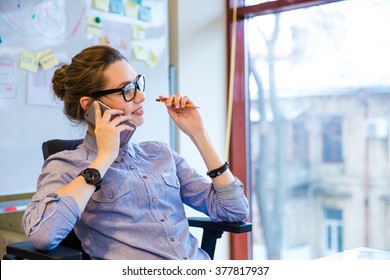 Happy Beautiful Young Business Woman In Glasses Sitting And Talking On Cell Phone In Office