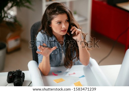 Happy beautiful young business woman sitting and talking on cell phone in office. Casual businesswoman in office.
