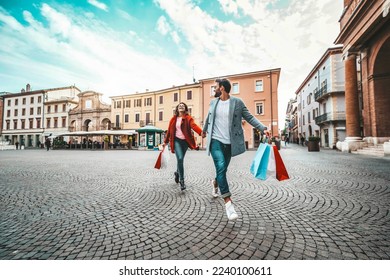 Happy beautiful young couple holding shopping bags walking on city street - Two loving tourists having fun on weekend vacation - Holidays and shopping concept - Powered by Shutterstock