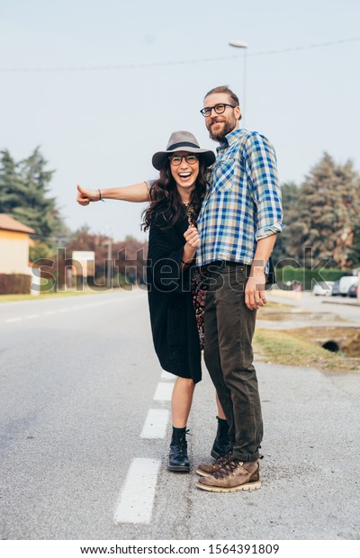 Happy beautiful young couple\
outdoor hitchhiking having fun throughfare - journey, transport\
concept