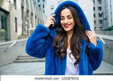 Happy Beautiful Young Cute Woman In Blue Vegan And Faux Fur Coat Is Posing On Urban City Background. Fashion Trendy Style Clothes