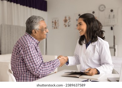 Happy beautiful young geriatric practitioner woman and senior Indian patient man shaking hands in clinic office, meeting for consultation, examination, talking, smiling, laughing - Powered by Shutterstock