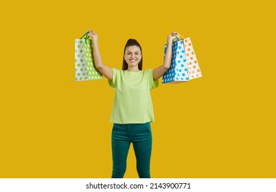 Happy beautiful young girl in casual outfit standing isolated on bright yellow background, smiling and showing shopping bags with many purchases. Cheerful attractive woman enjoying holiday season sale - Shutterstock ID 2143900771